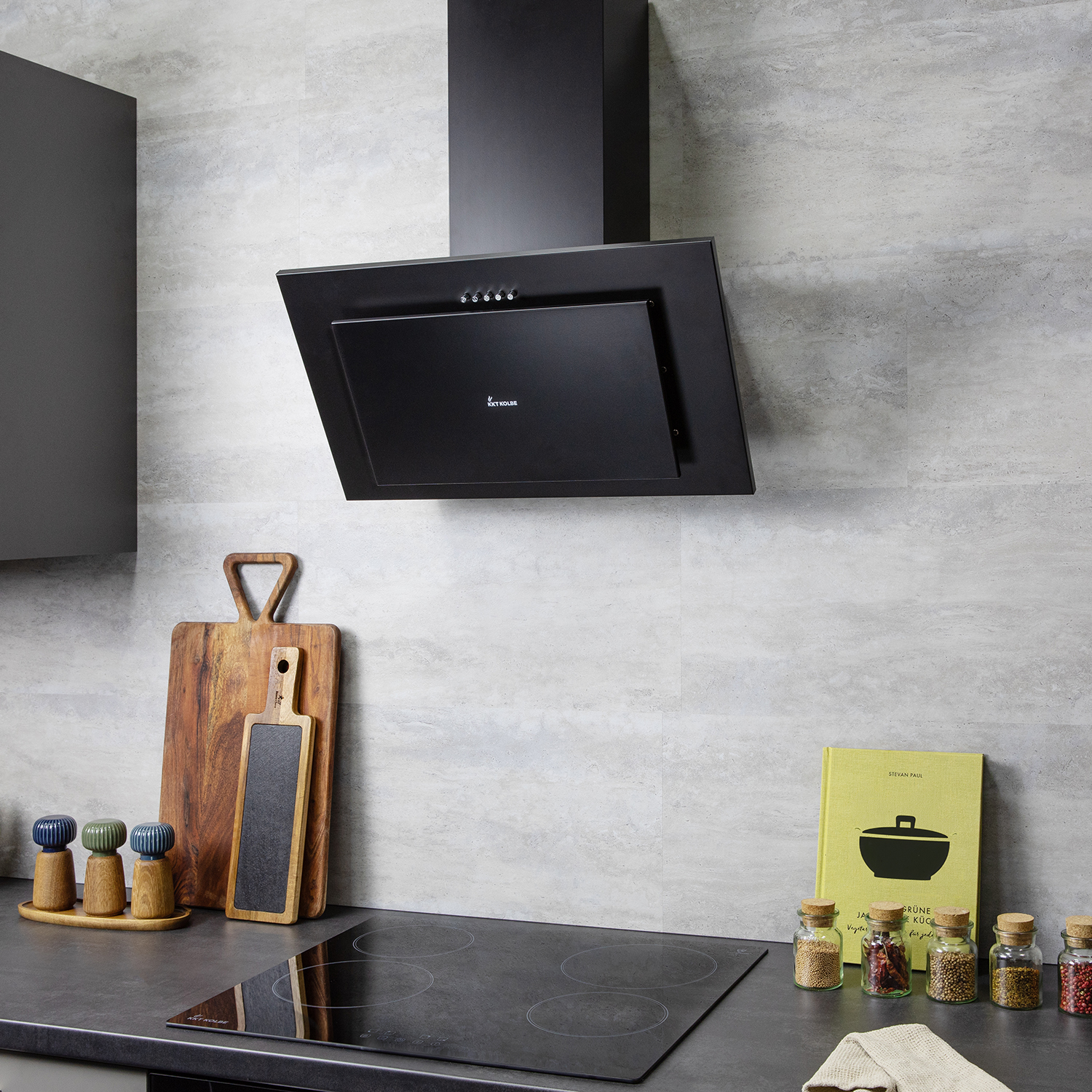 Una cucina moderna con cappa nera, piano cottura a induzione, taglieri in legno, barattoli di spezie e libro.
