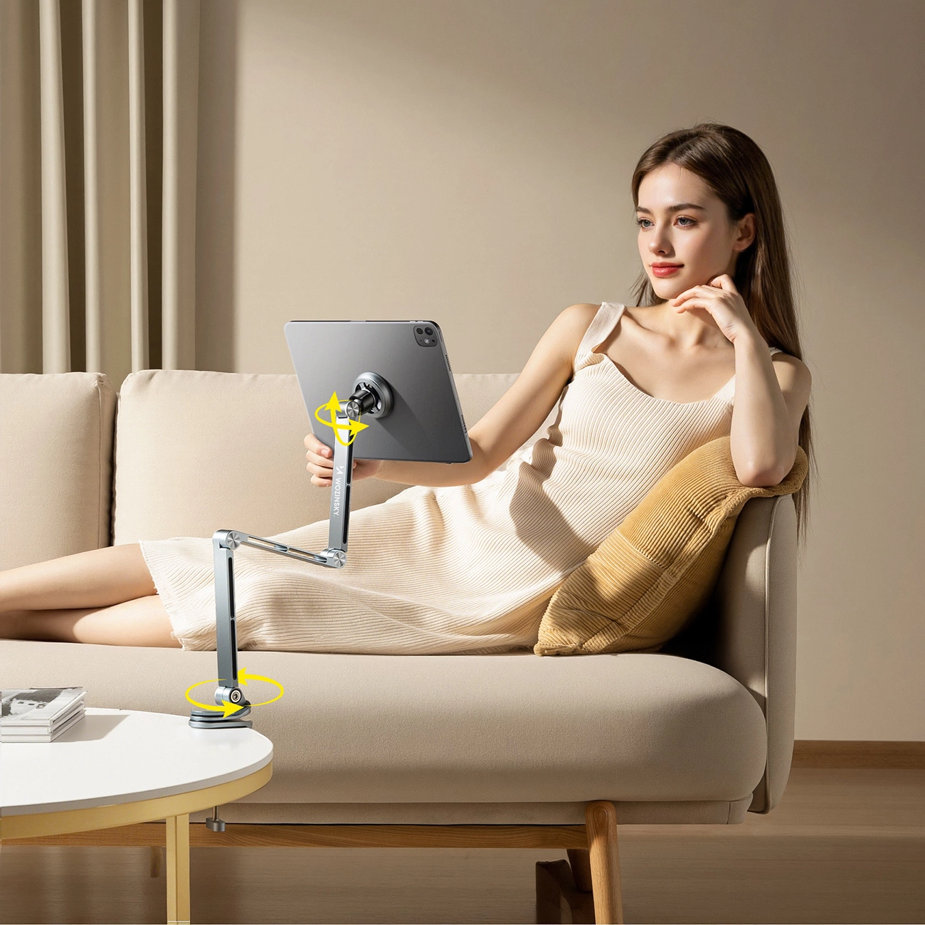 Una donna si rilassa su un divano beige usando un tablet su un braccio articolato al tavolino.