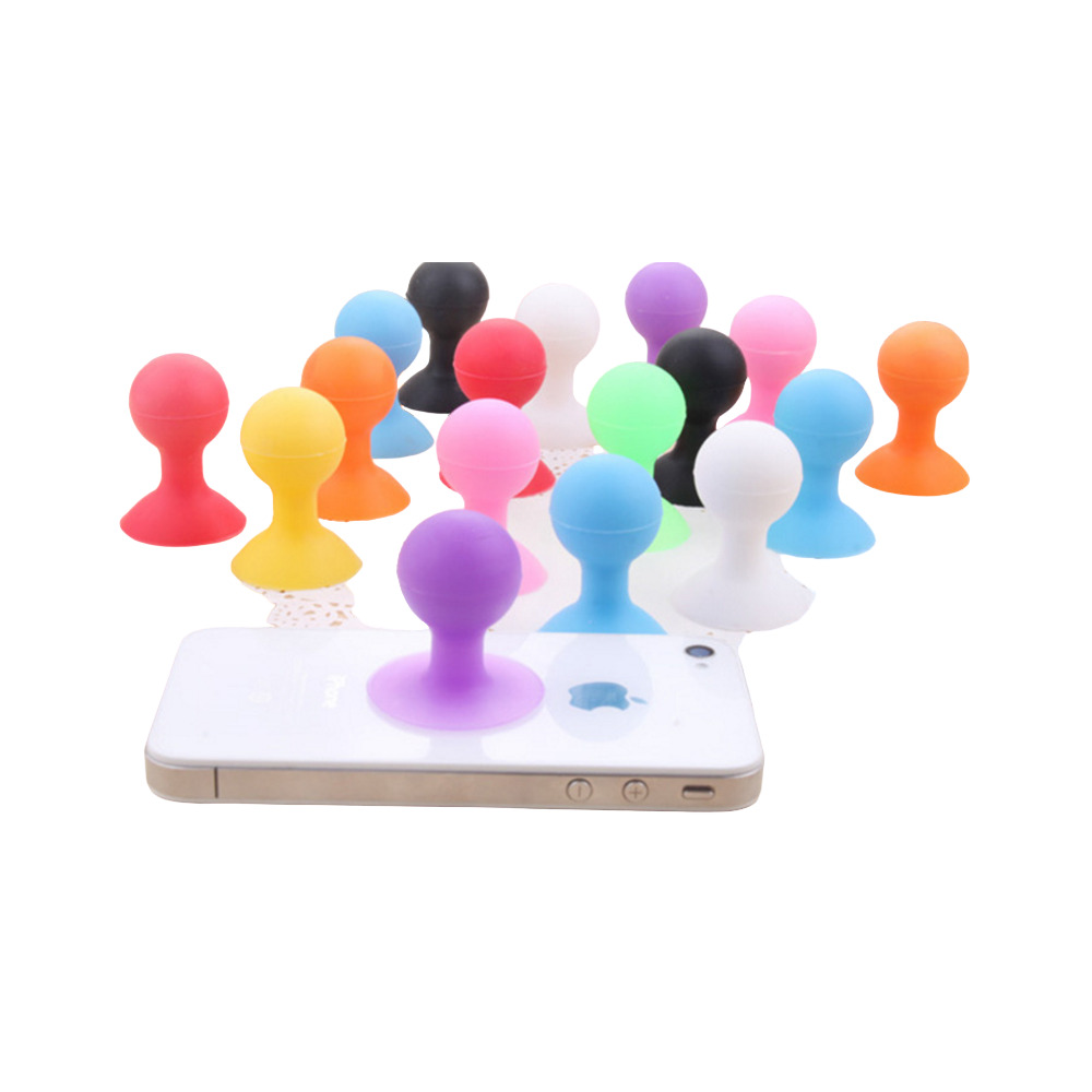 Molti supporti con ventosa in silicone colorati sono disposti su una superficie bianca, uno attaccato a un telefono.