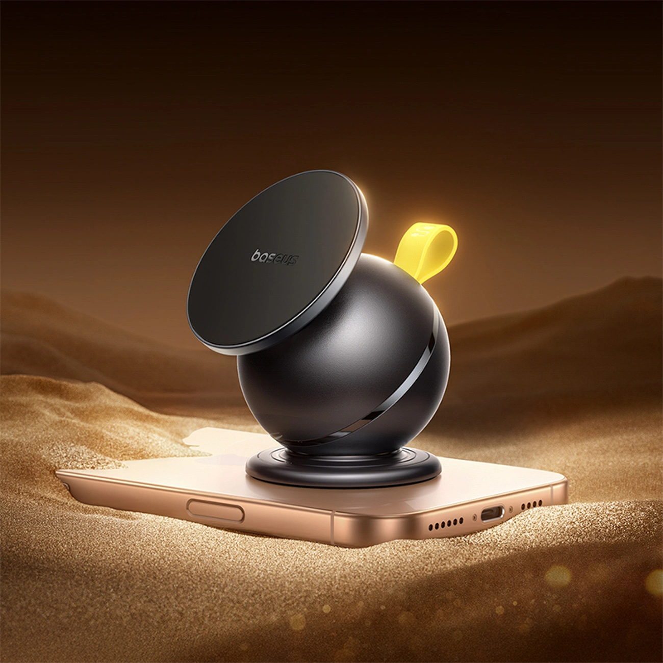 Un supporto magnetico sferico nero Baseus su uno smartphone dorato in un paesaggio desertico sabbioso e caldo.