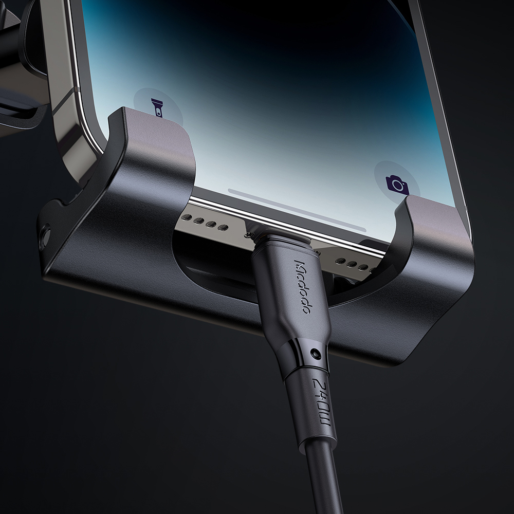 Uno smartphone in un supporto viene caricato con un cavo nero su sfondo scuro.