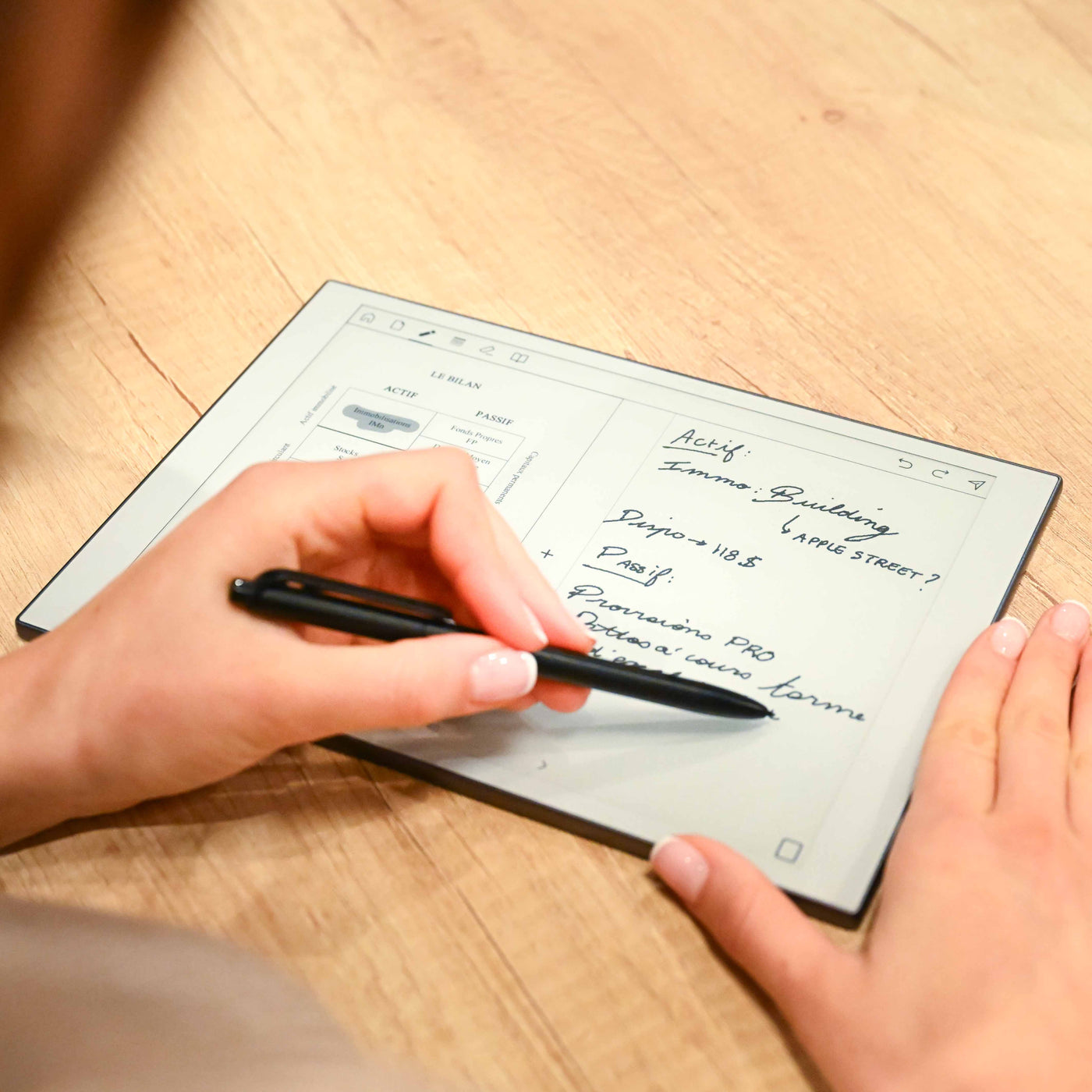 Una persona escribe notas con un bolígrafo negro en una pantalla de tableta digital sobre un escritorio.