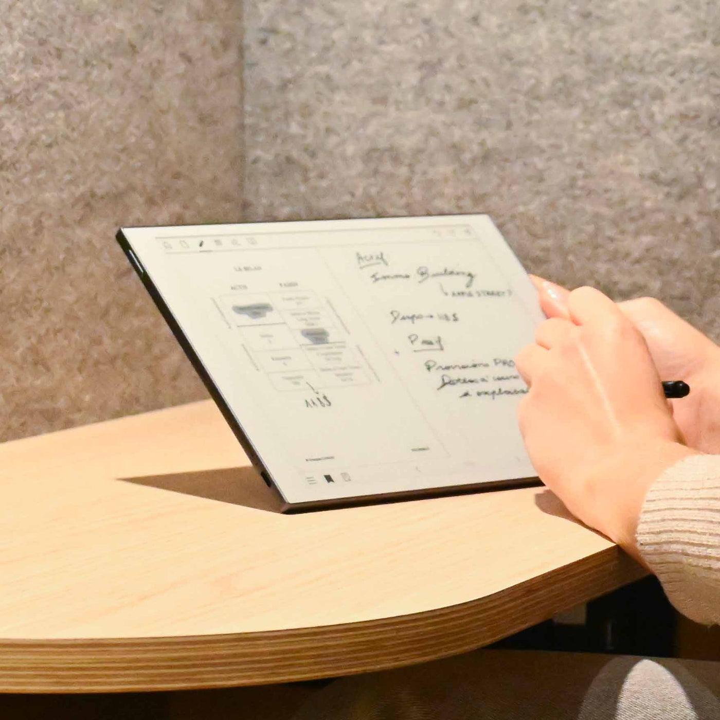 Una persona escribe con un lápiz óptico en una tableta electrónica sobre una mesa de madera.