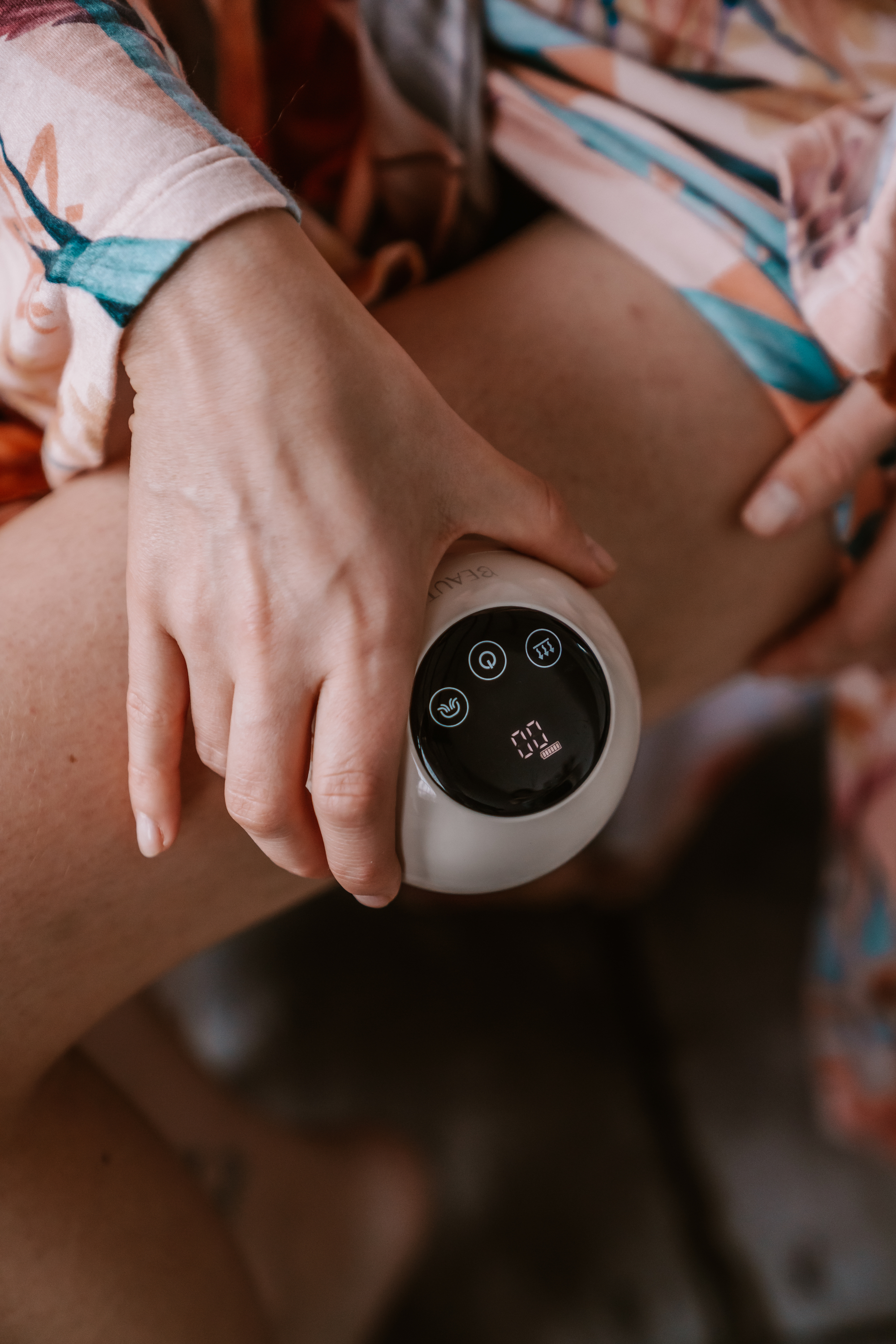 Una mano tiene un dispositivo cosmetico rotondo bianco con schermo LED nero su una gamba.