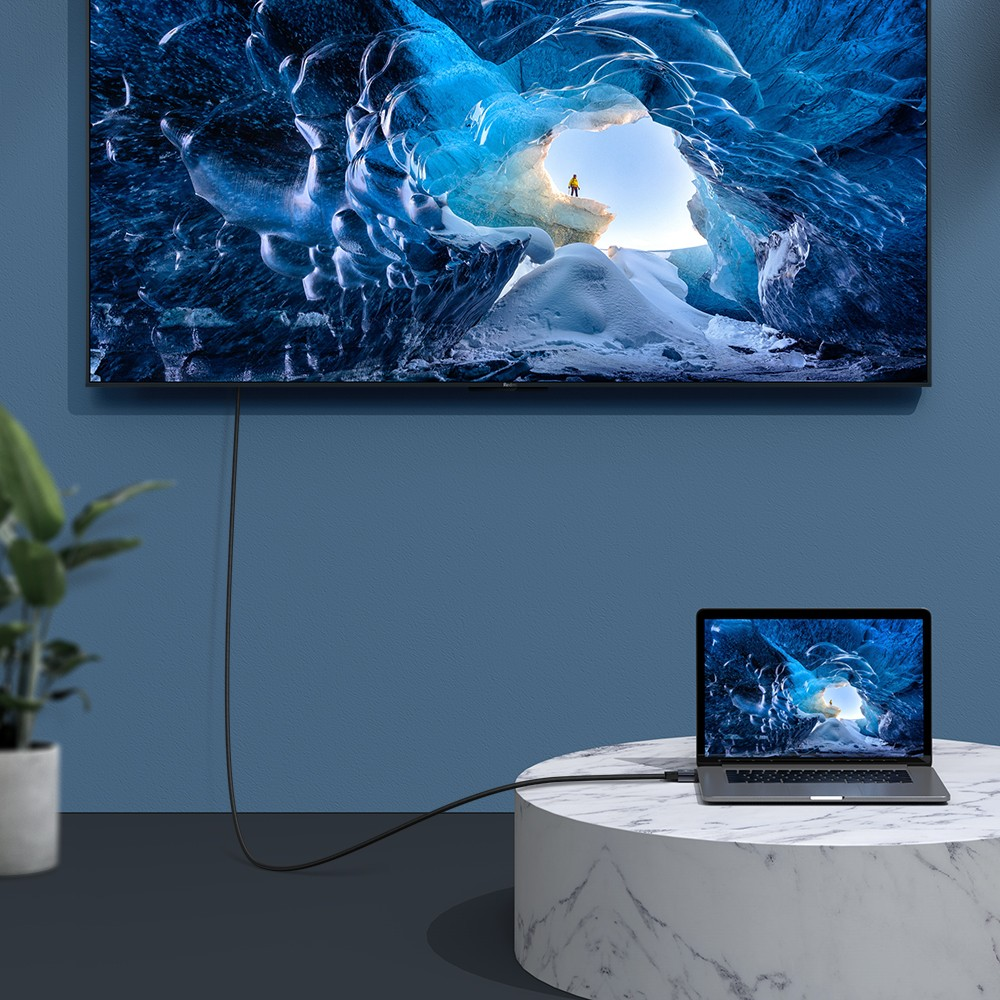 Un computer portatile è collegato tramite un cavo a una grande TV a parete, entrambi mostrano la stessa immagine di un ghiacciaio.