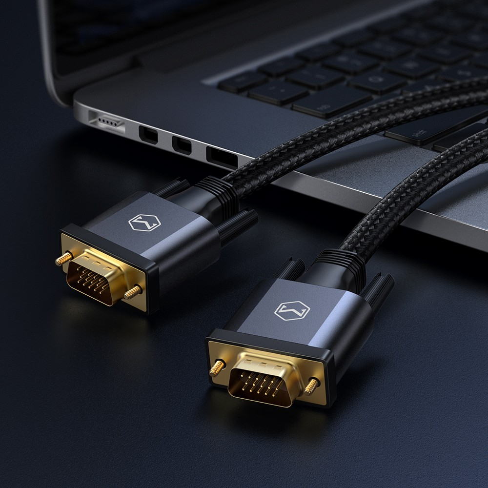 Due cavi VGA intrecciati con connettori placcati in oro poggiano su una superficie scura davanti a un computer portatile.