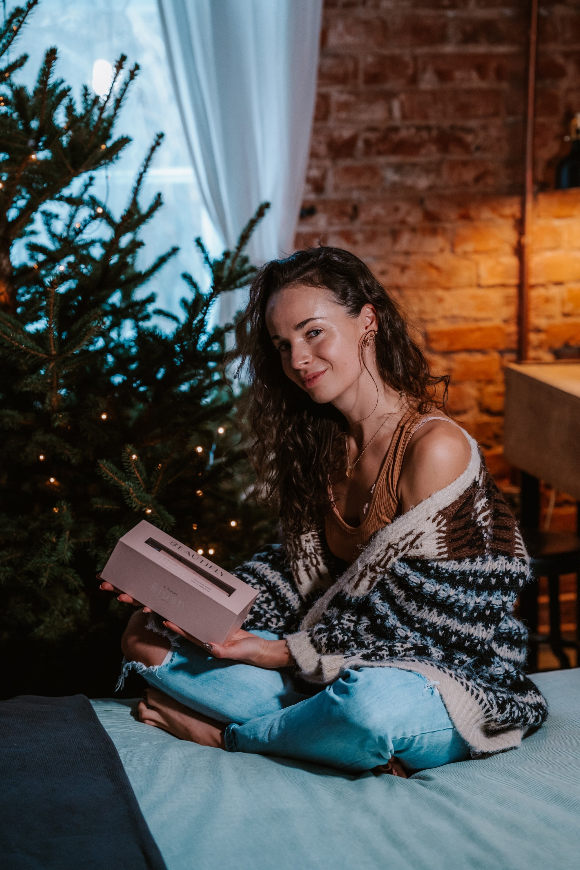 Una donna è seduta che tiene una confezione regalo rosa vicino a un albero di Natale.