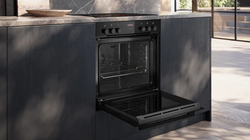 Schwarzer Backofen mit geöffneter Tür in einer modernen Küche mit dunklen Fronten.