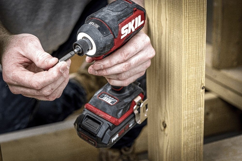 Una persona inserisce un inserto in un avvitatore a impatto cordless Skil rosso e nero.