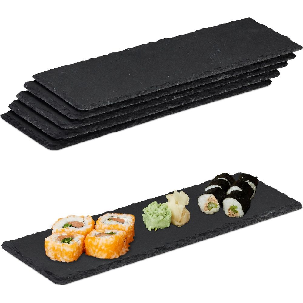 Stapel schwarzer Schieferplatten und eine einzelne Platte mit Sushi, Wasabi und Ingwer auf weißem Hintergrund.