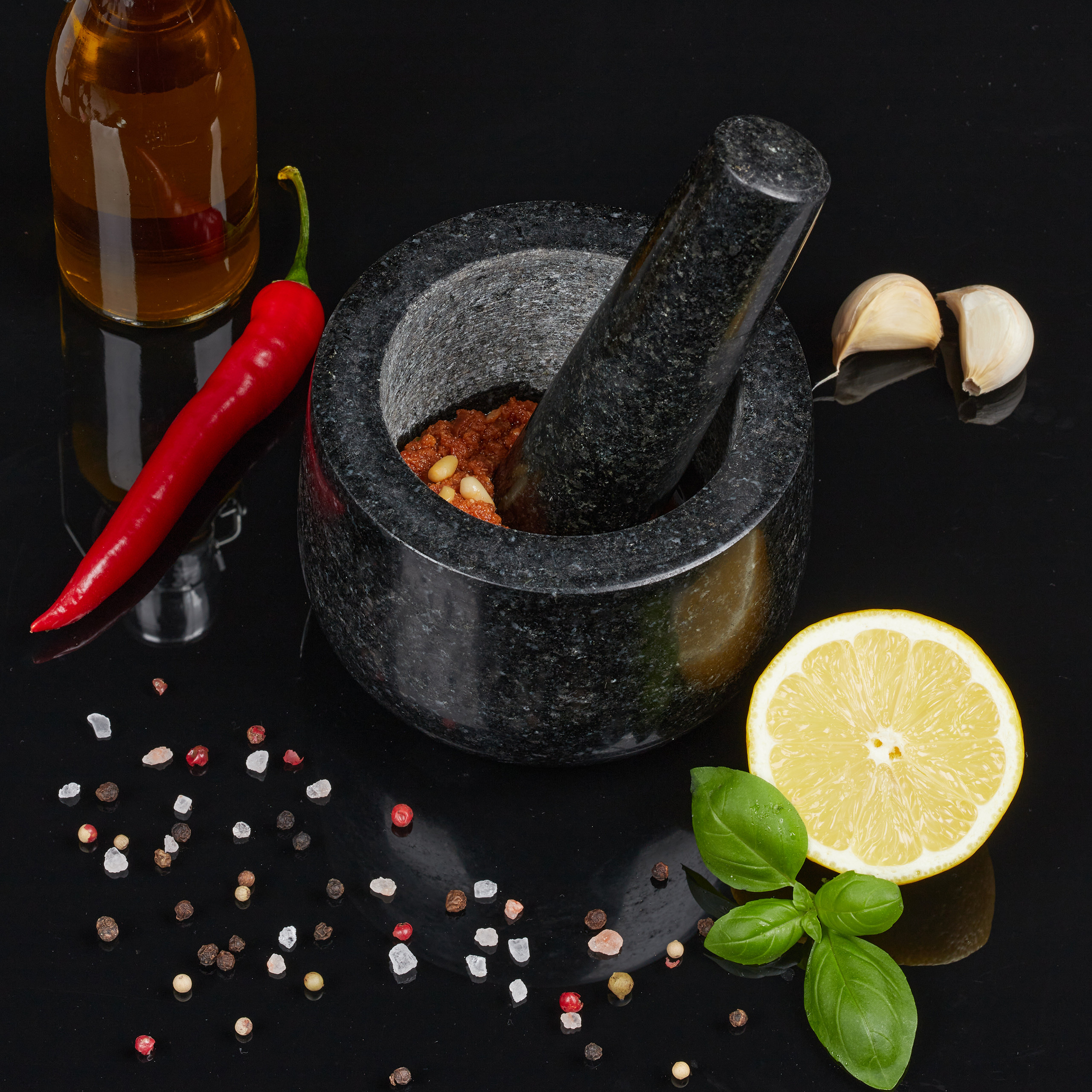 Mörser mit Paste, roter Chili, Ölflasche, Knoblauch, Zitrone und Gewürzen auf schwarzem Grund.