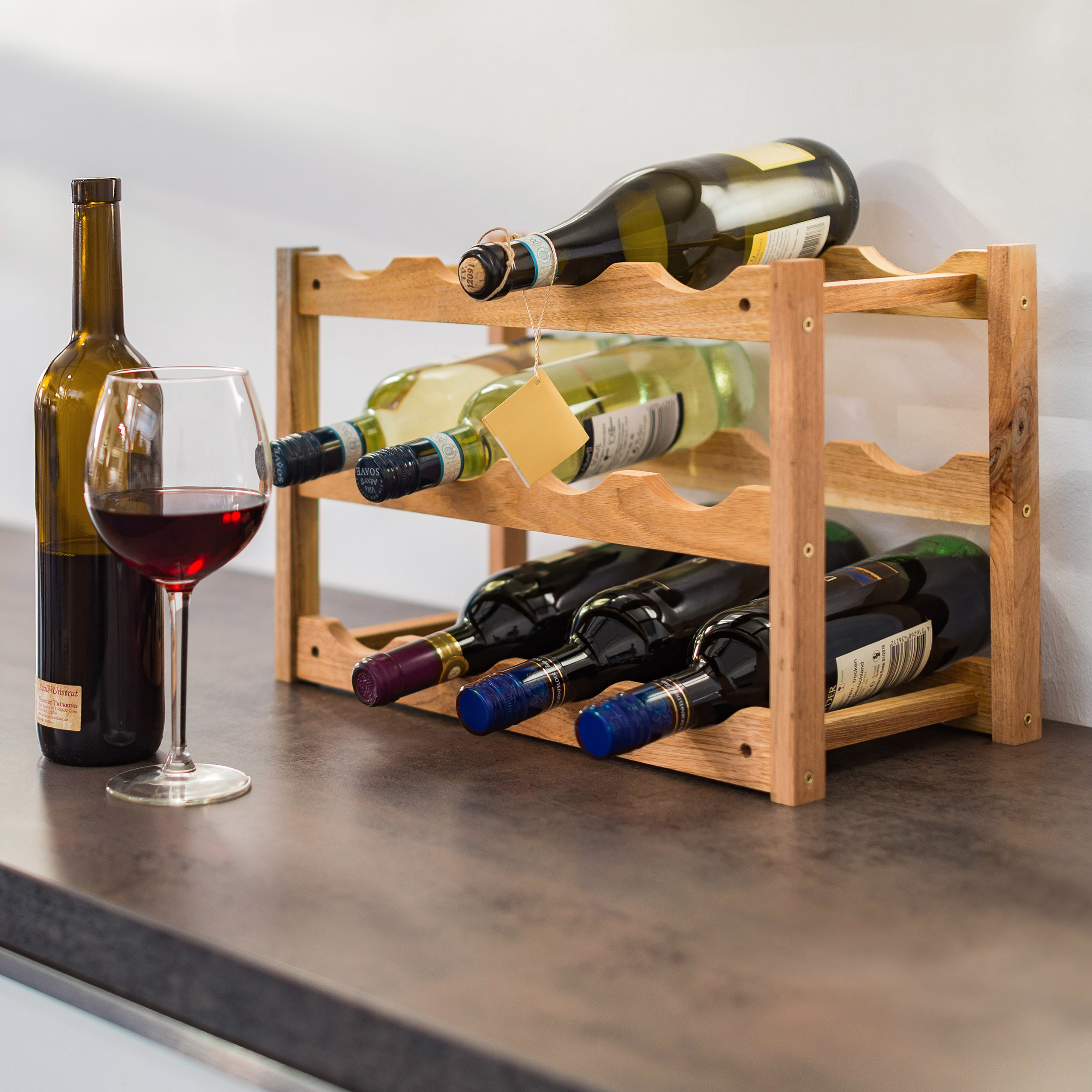 Ein hölzernes Weinregal mit mehreren Weinflaschen, eine Weinflasche und ein Glas mit Rotwein stehen auf der Theke.