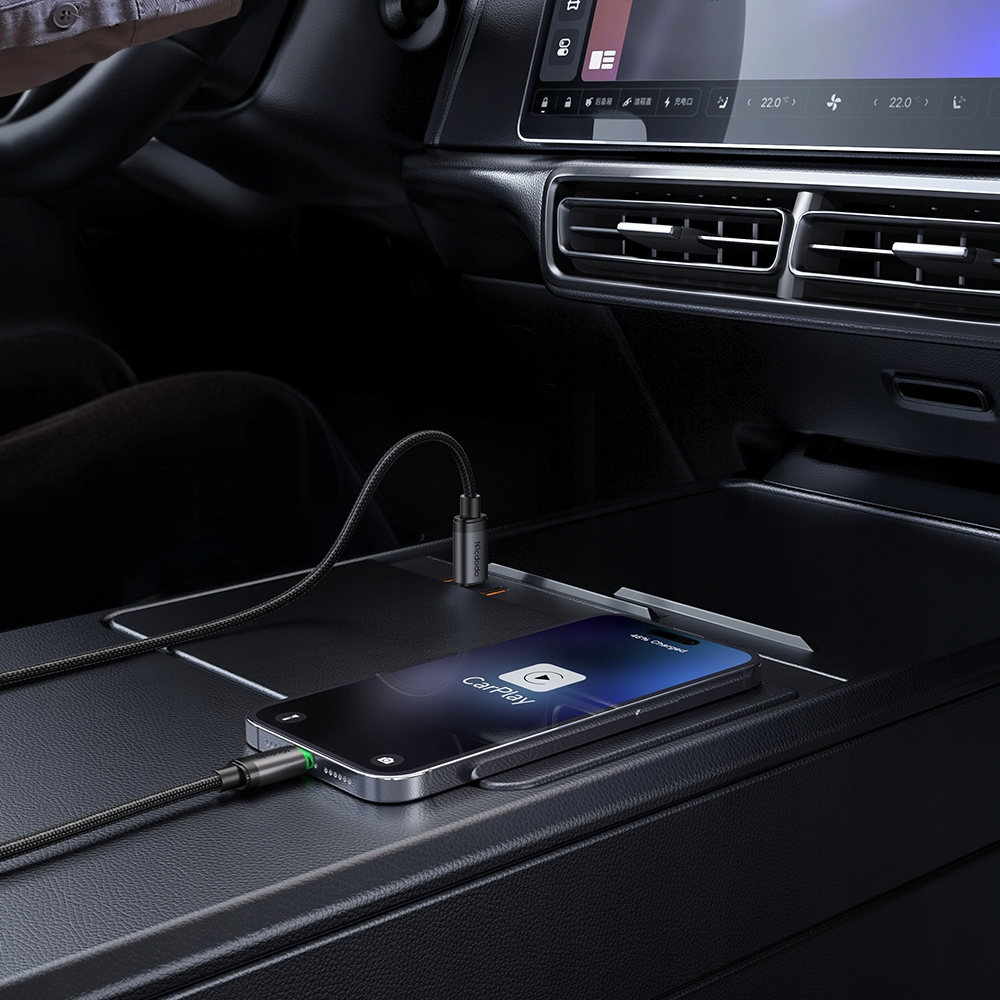 Uno smartphone collegato con un cavo intrecciato è sulla console di un'auto, mostrando CarPlay.