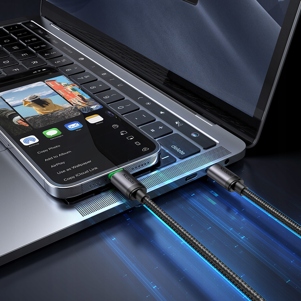 Smartphone e laptop collegati con cavi, con effetto di luce blu su sfondo scuro.