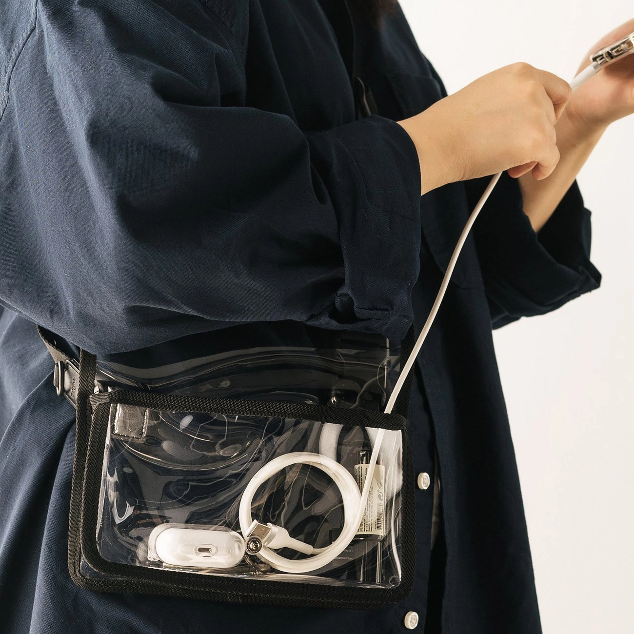 Una persona indossa una borsa a tracolla trasparente contenente cavi e auricolari, mentre tiene uno smartphone.