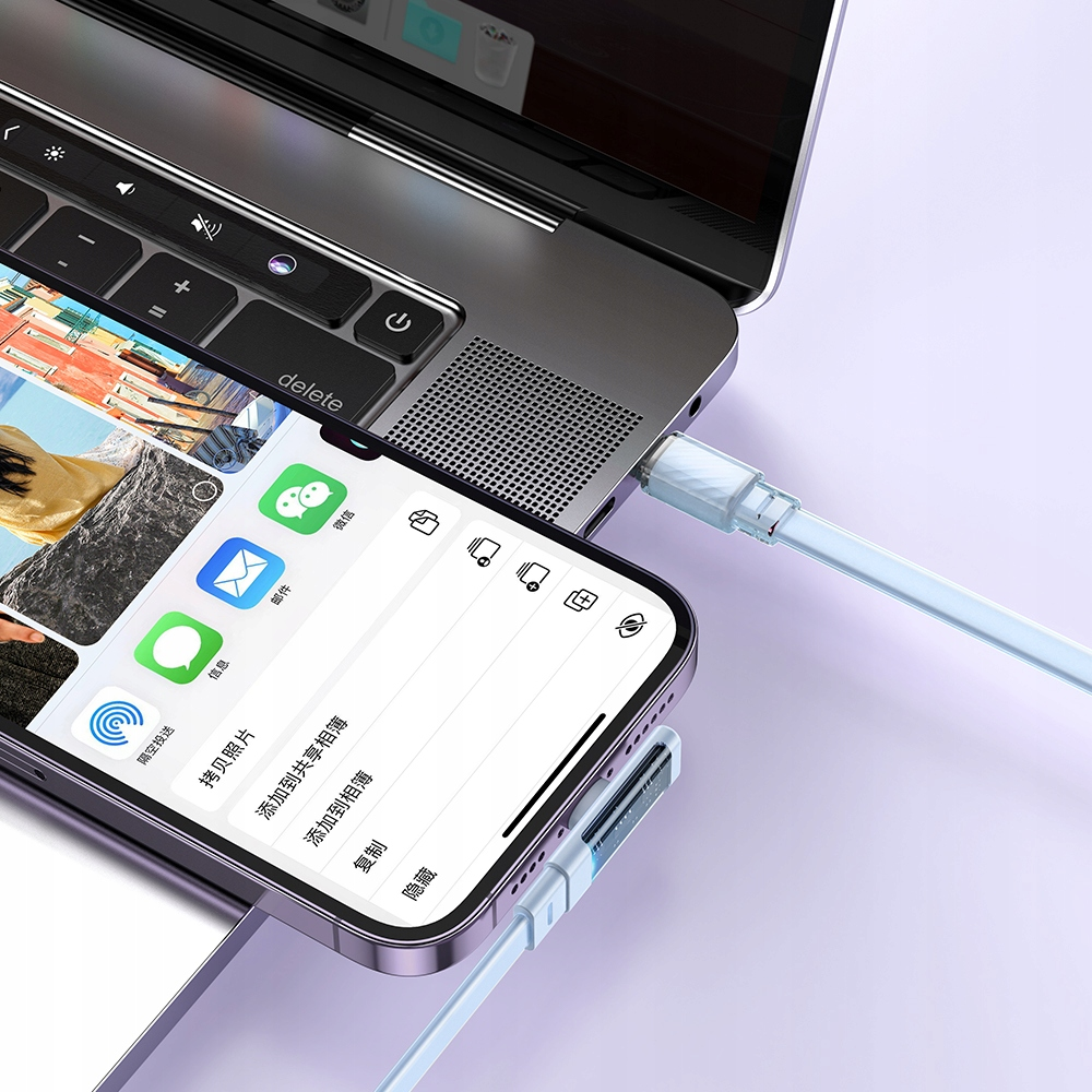 Uno smartphone e un computer portatile collegati con cavi azzurri su una superficie viola chiaro.