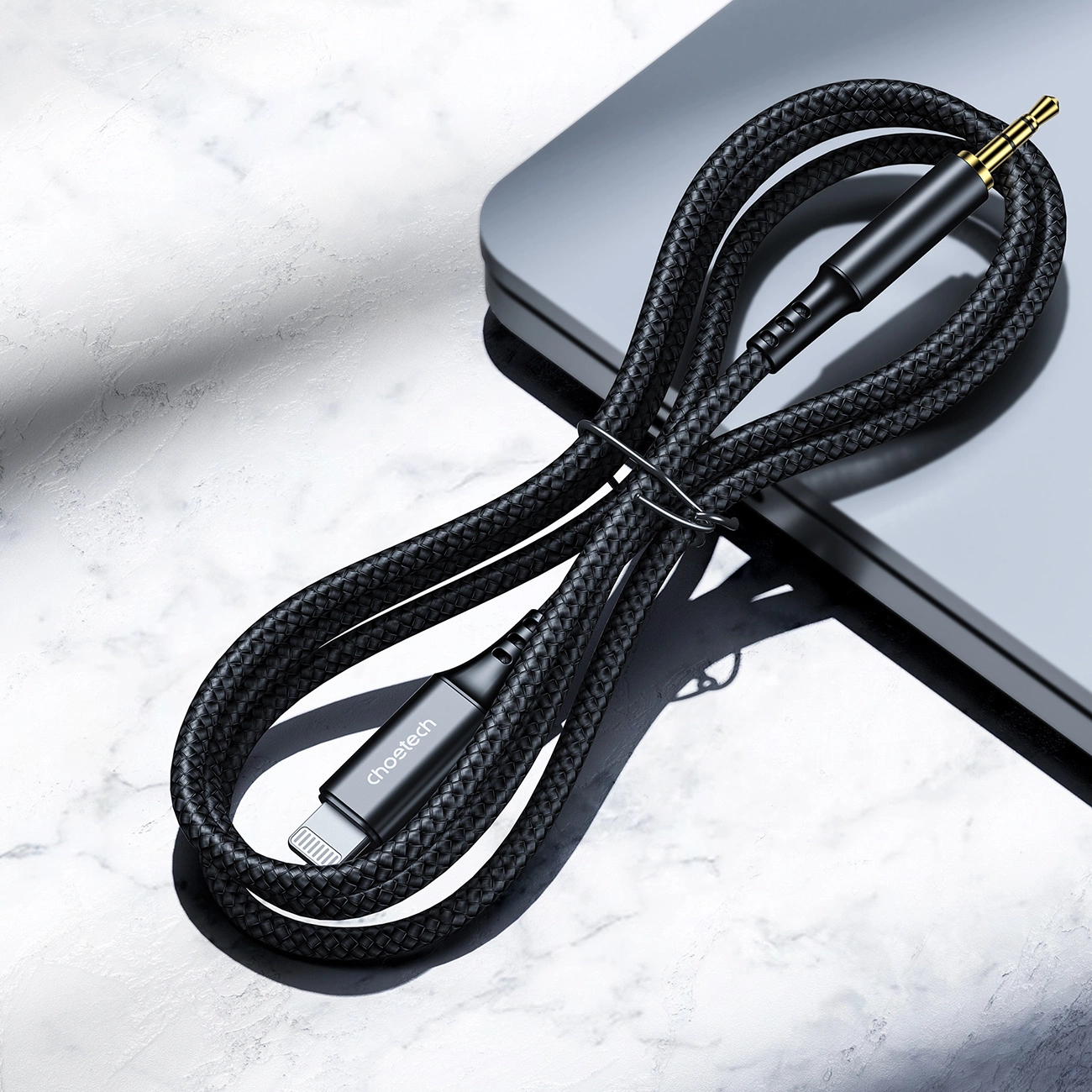 Un cavo aux nero intrecciato con connettori Lightning e da 3,5 mm su una superficie grigia.