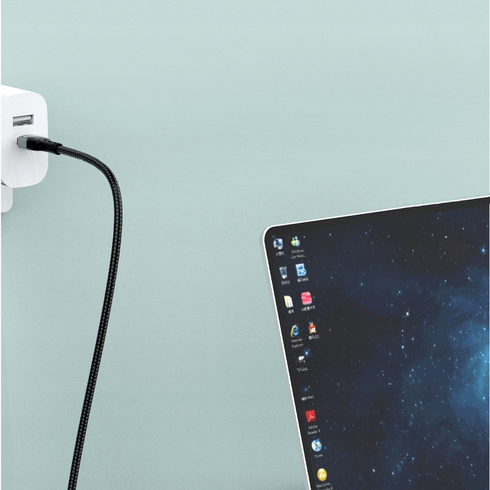 Un cavo intrecciato nero collegato a un caricatore a muro bianco e un laptop su sfondo chiaro.
