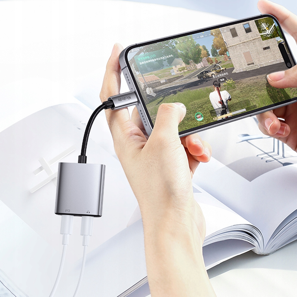 Persona che tiene in mano uno smartphone grigio con adattatore audio e di ricarica mentre gioca.