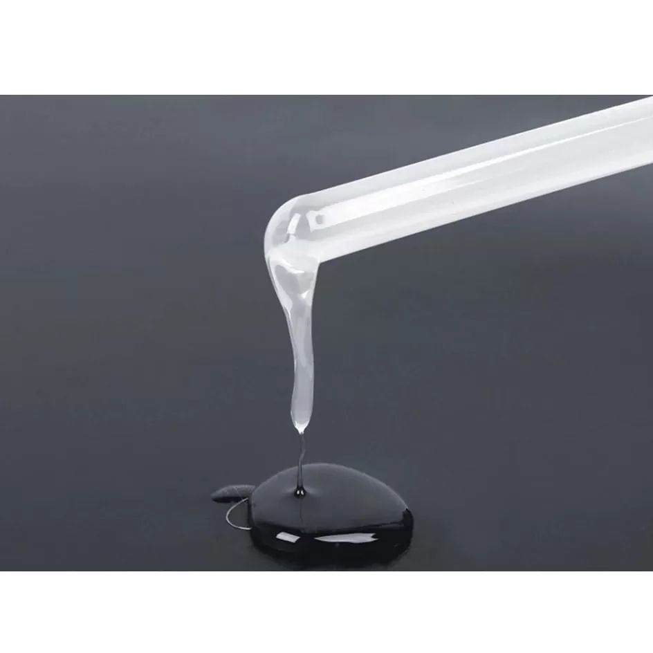Eine Pipette tropft klare Flüssigkeit auf eine schwarze Oberfläche.