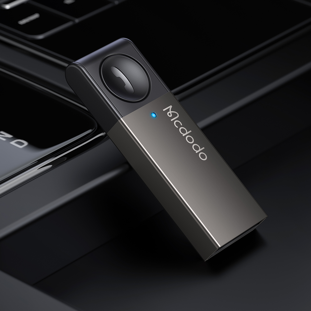 Un elegante adattatore USB Mcdodo nero con una luce LED blu e un grande pulsante funzione poggia su una superficie lucida.