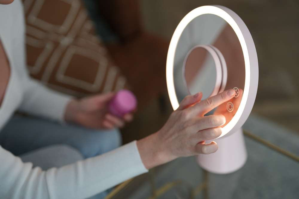 Kobieta dotyka podświetlanego panelu dotykowego na różowym lusterku do makijażu.