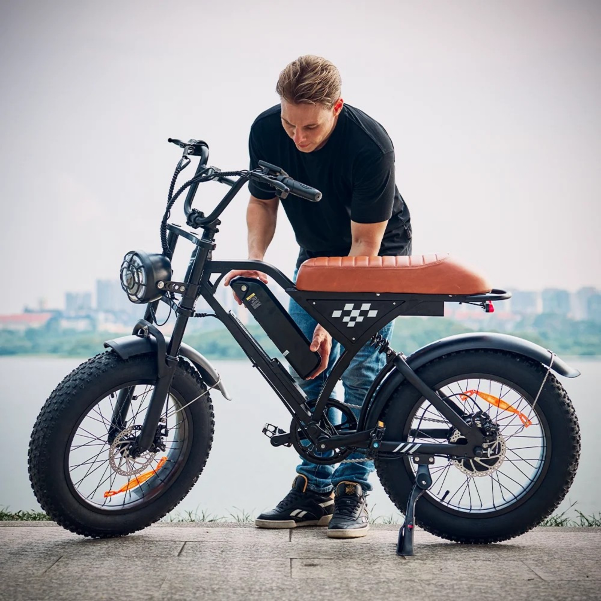 Mężczyzna instaluje czarną baterię w swoim rowerze elektrycznym na tle jeziora i miasta.