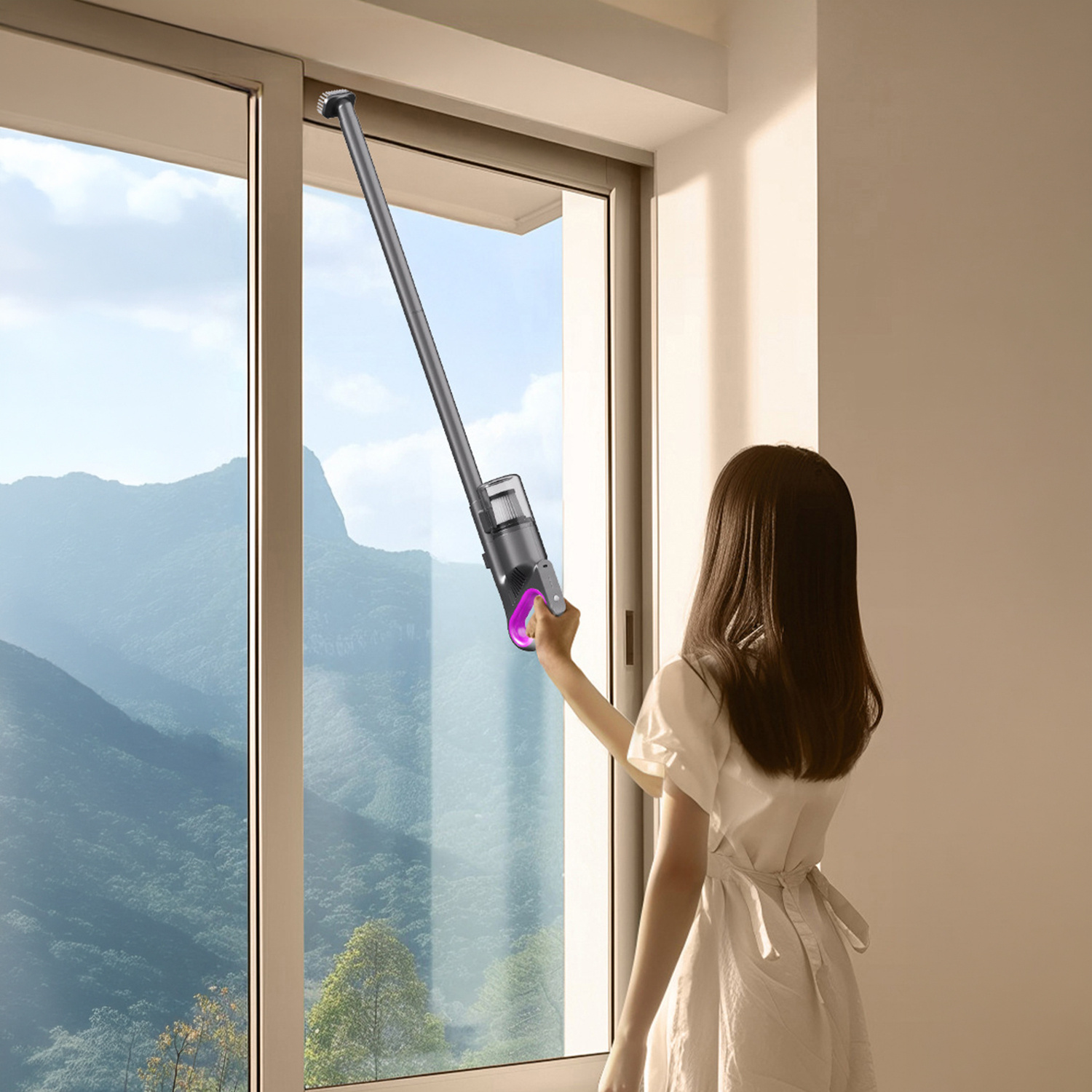 Una mujer usa una aspiradora de mano para limpiar una gran ventana con vista a montañas verdes.