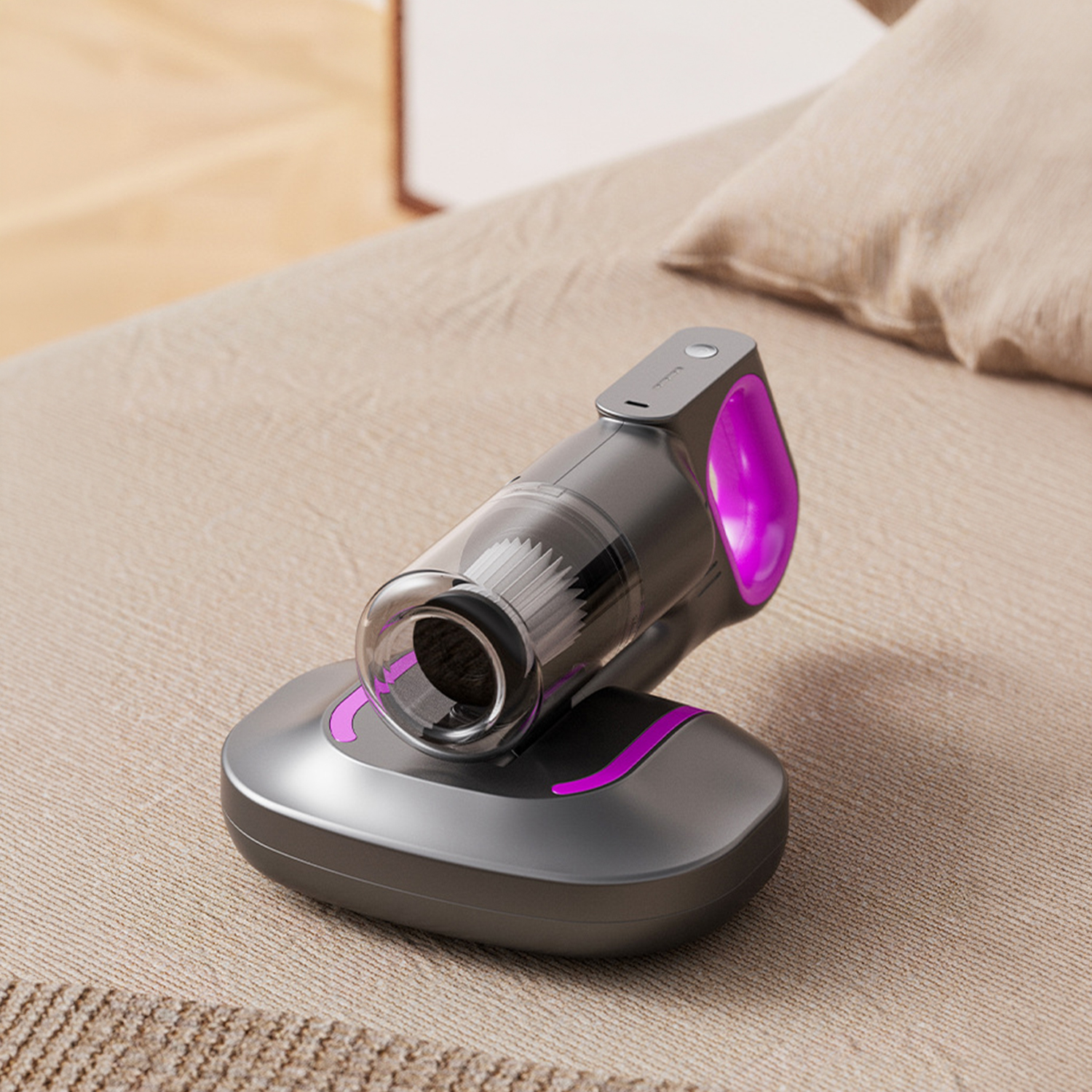 Una aspiradora de mano gris con detalles en rosa brillante reposa en un sofá de tela beige junto a una almohada.