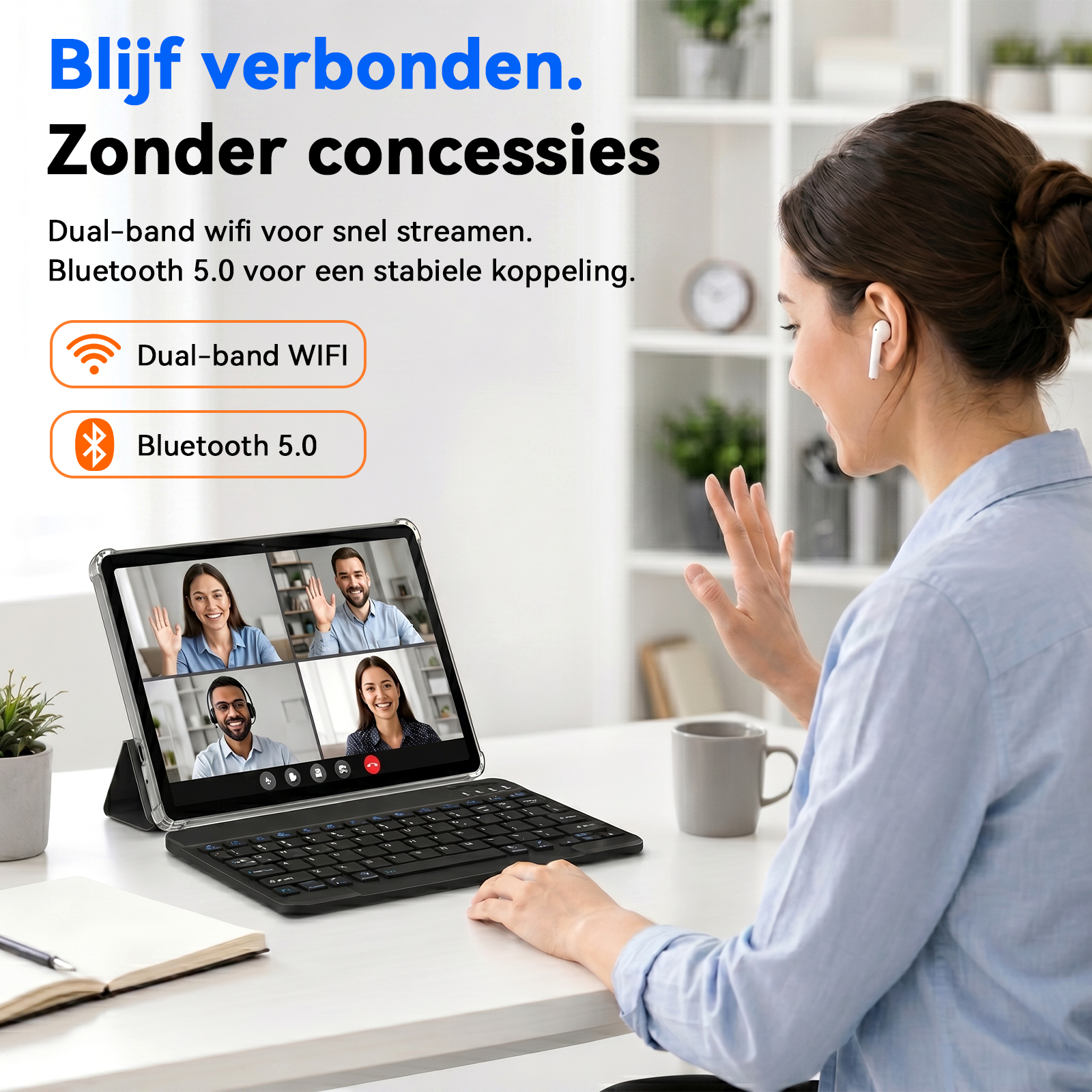 A woman sits at a desk, waving during a video call on a tablet with a keyboard.