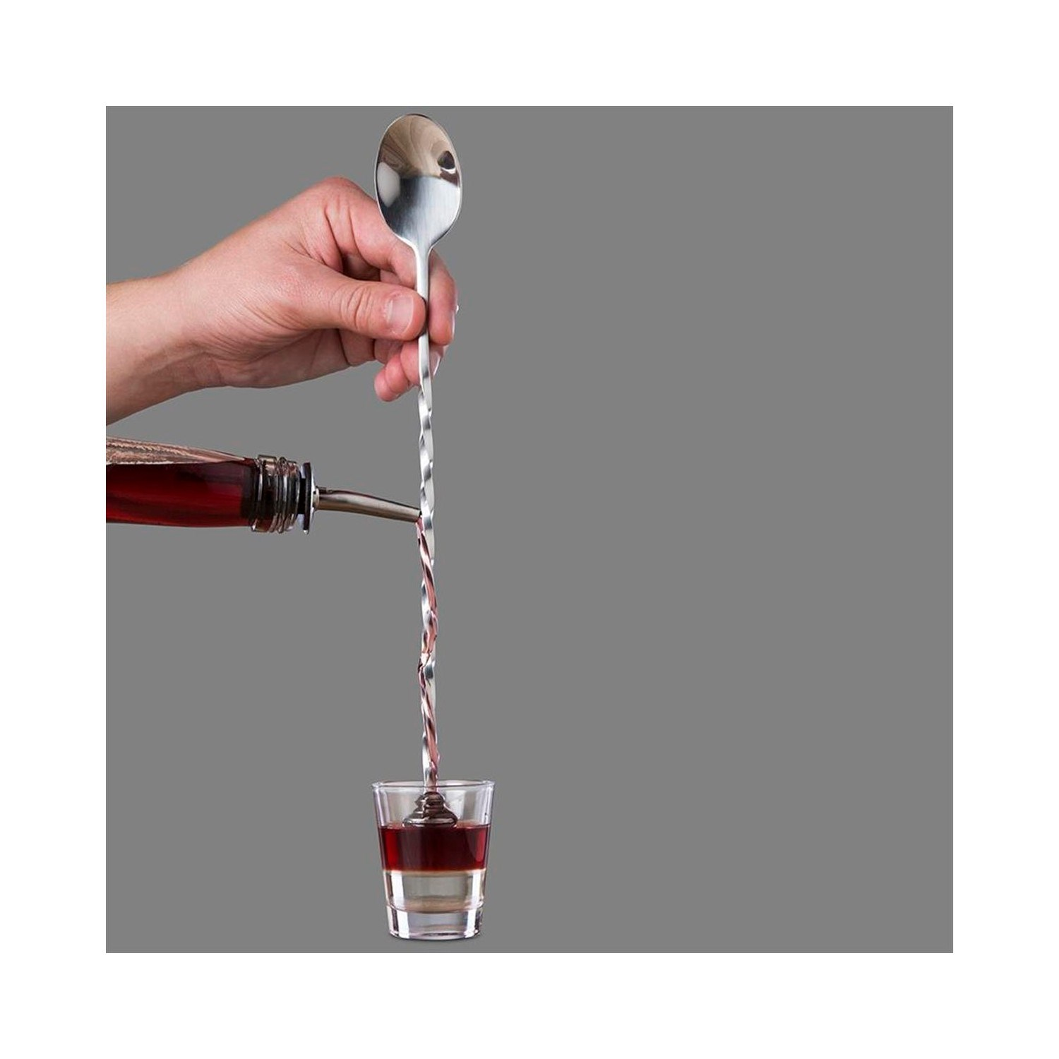 Bir el barmen kaşığı tutarken kırmızı likör bir shot bardağına dökülüyor.
