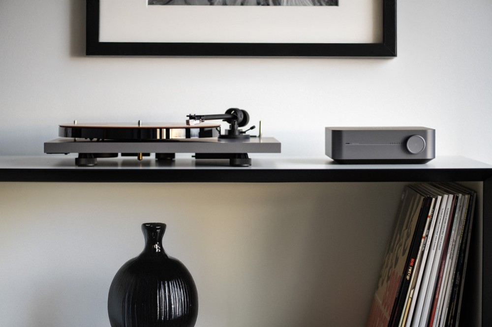 Gramofon i wzmacniacz na półce, z czarnym wazonem i płytami winylowymi.