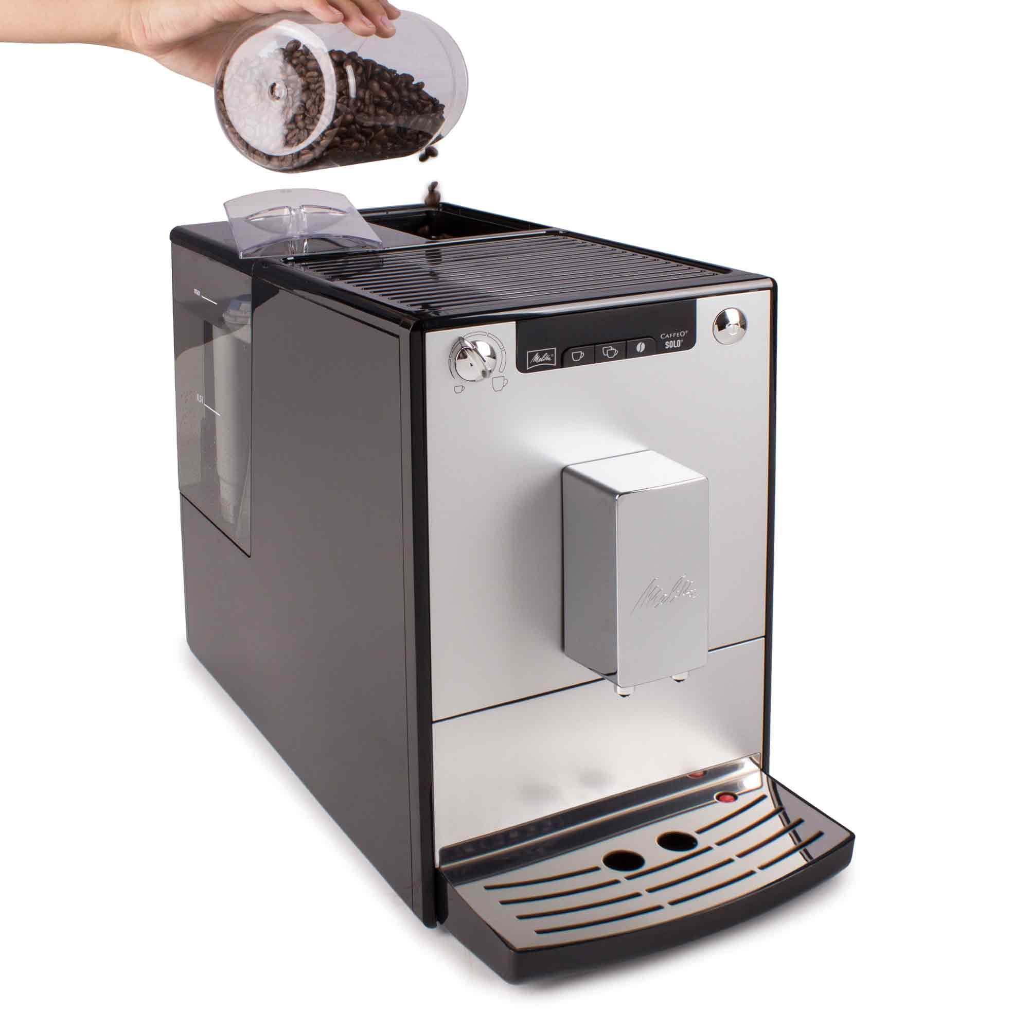 Una mano versa chicchi di caffè da un contenitore trasparente nella tramoggia superiore di una moderna macchina da caffè.