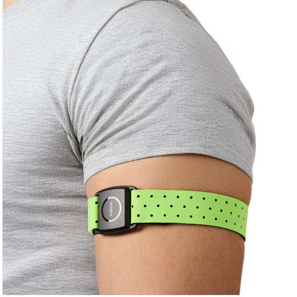 Persona che indossa una fascia fitness verde con sensore nero sul braccio sopra una maglietta grigia.