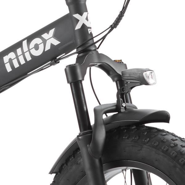 Primo piano di una e-bike Nilox nera con forcella anteriore, faro e pneumatico tassellato su sfondo bianco.