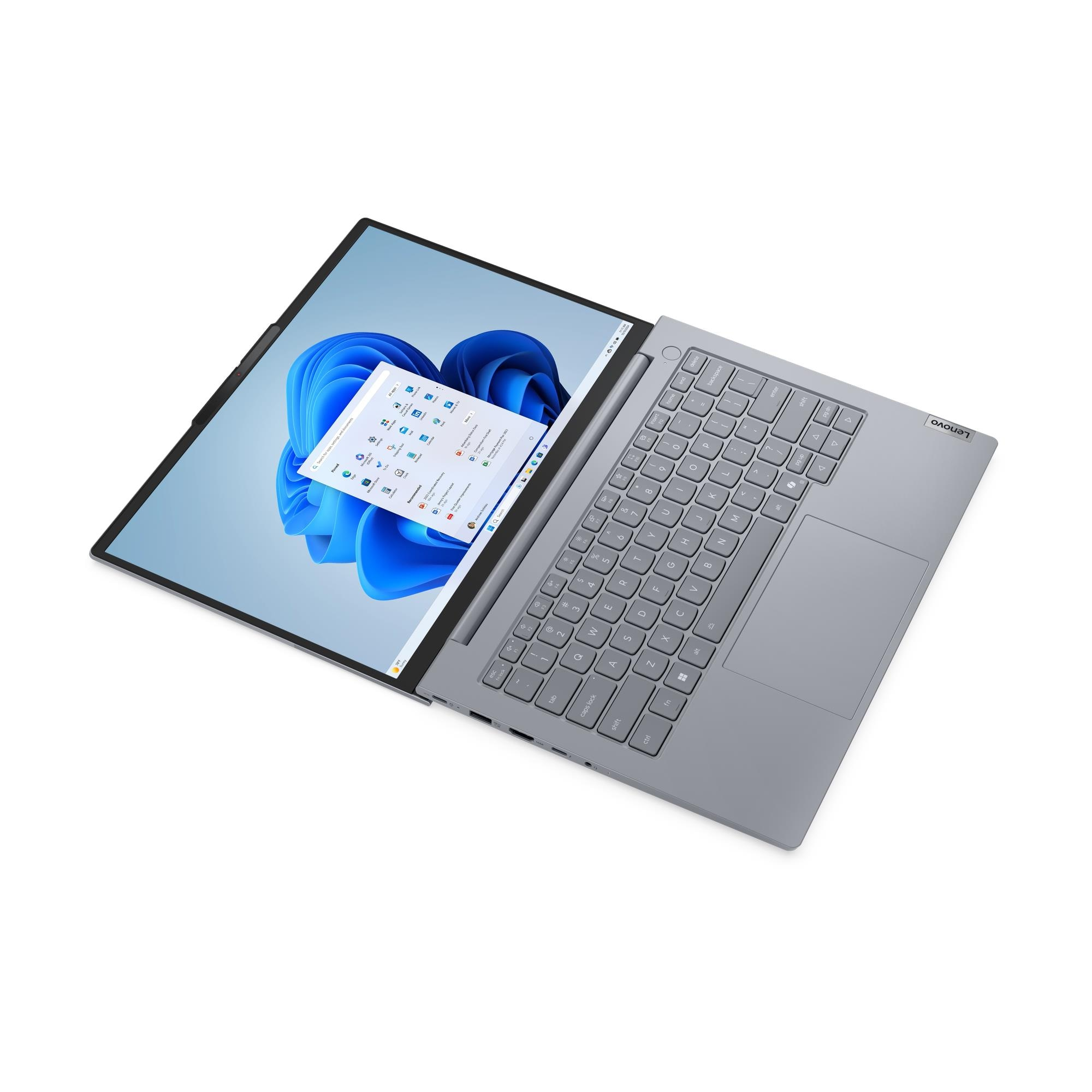 Beyaz arka planda gri bir dizüstü bilgisayar, mavi duvar kağıdıyla Windows 11 başlangıç ekranını gösterir.
