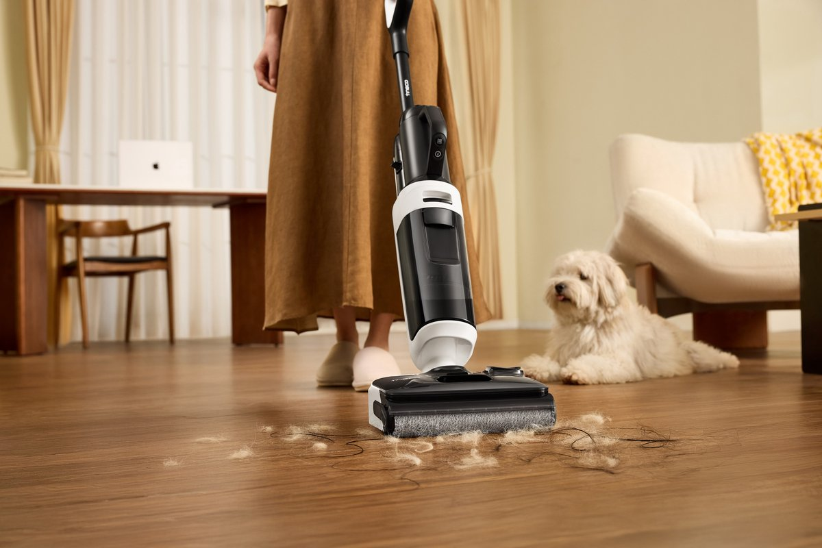 Una persona usa un pulitore per pavimenti in legno, con un cane sullo sfondo.