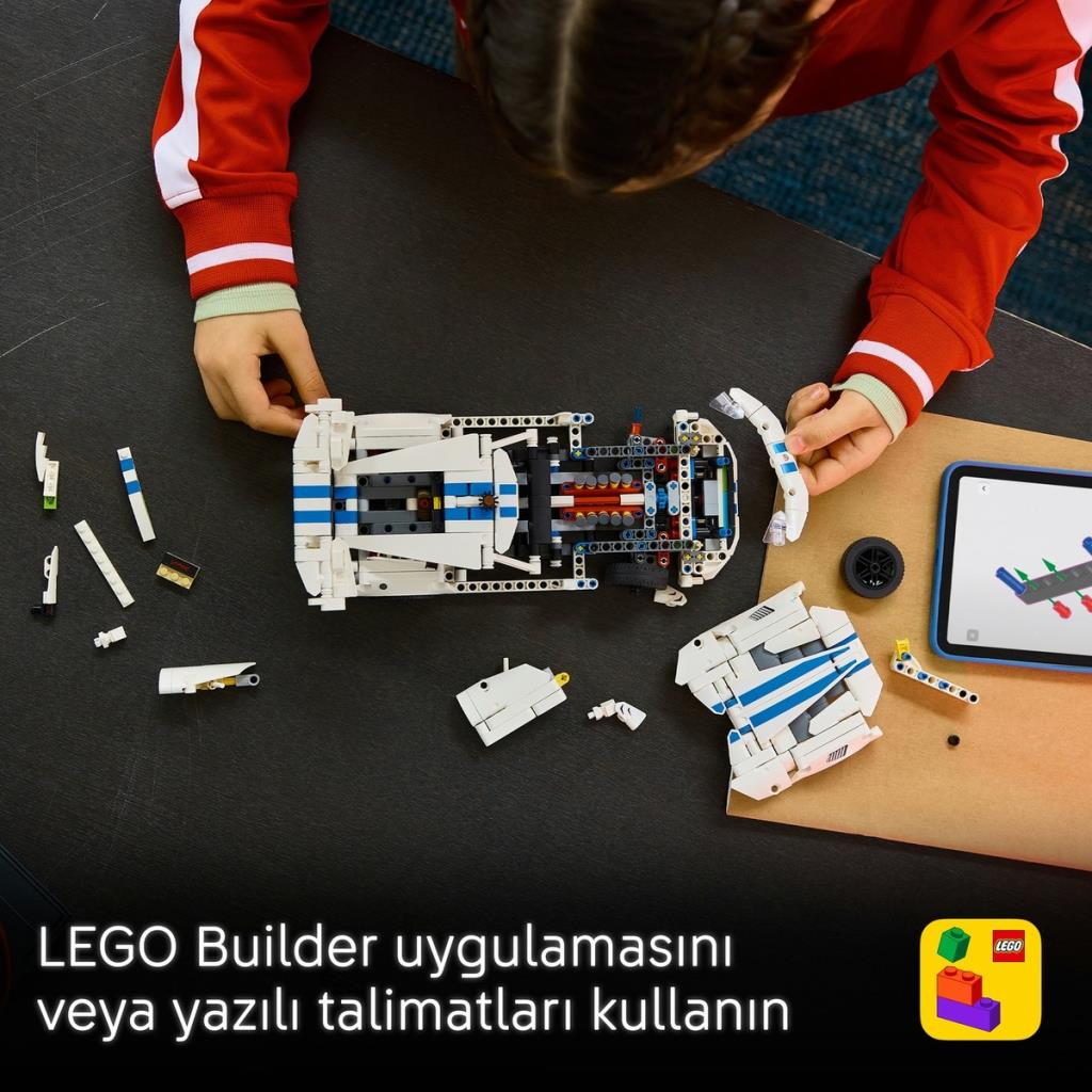 Bir çocuk tablete bakarak koyu renkli masa üzerinde beyaz ve mavi bir Lego araba yapıyor.