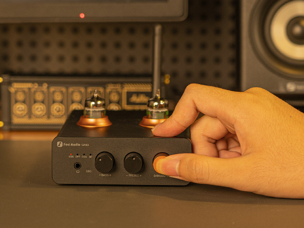 Ręka przekręca pokrętło głośności na czarnym wzmacniaczu lampowym Fosi Audio.
