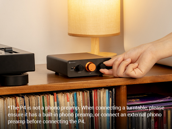 Eine Hand dreht den Regler eines schwarzen Audioverstärkers auf einem Holzregal mit Platten und Lampe.