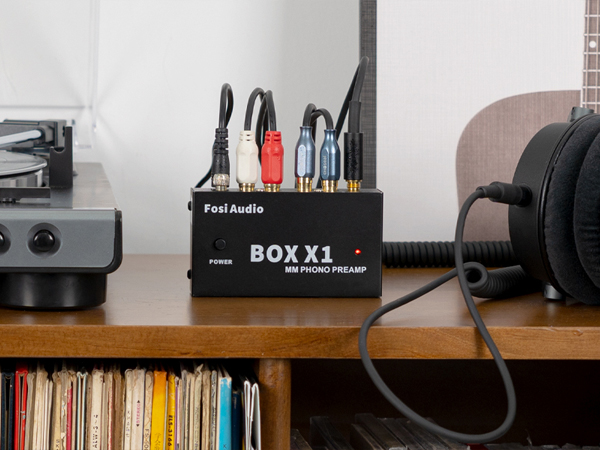 Przedwzmacniacz gramofonowy Fosi Audio BOX X1 na drewnianym biurku z kablami.