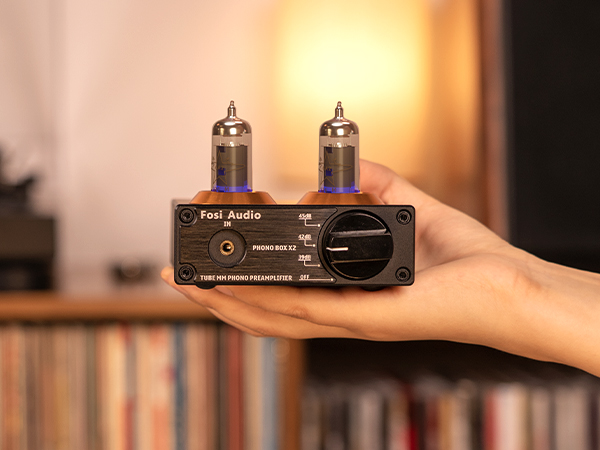 Una mano tiene un preamplificatore phono Fosi Audio nero con due tubi luminosi sopra.