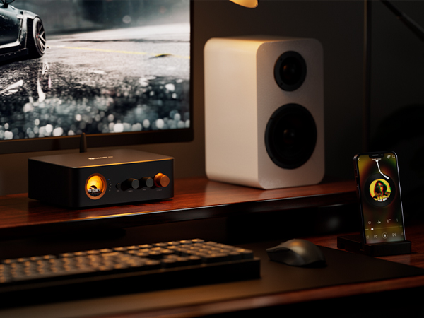 Biurko z amplitunerem audio, białym głośnikiem, monitorem, smartfonem, klawiaturą i myszką.