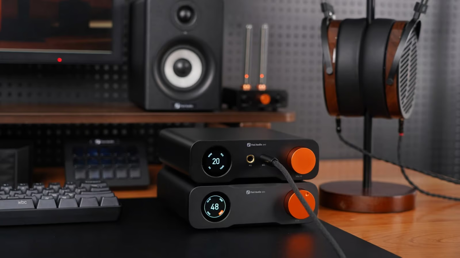 Stapelbare schwarze Fosi Audio Verstärker mit orangen Knöpfen und digitalen Displays auf einem Holztisch.