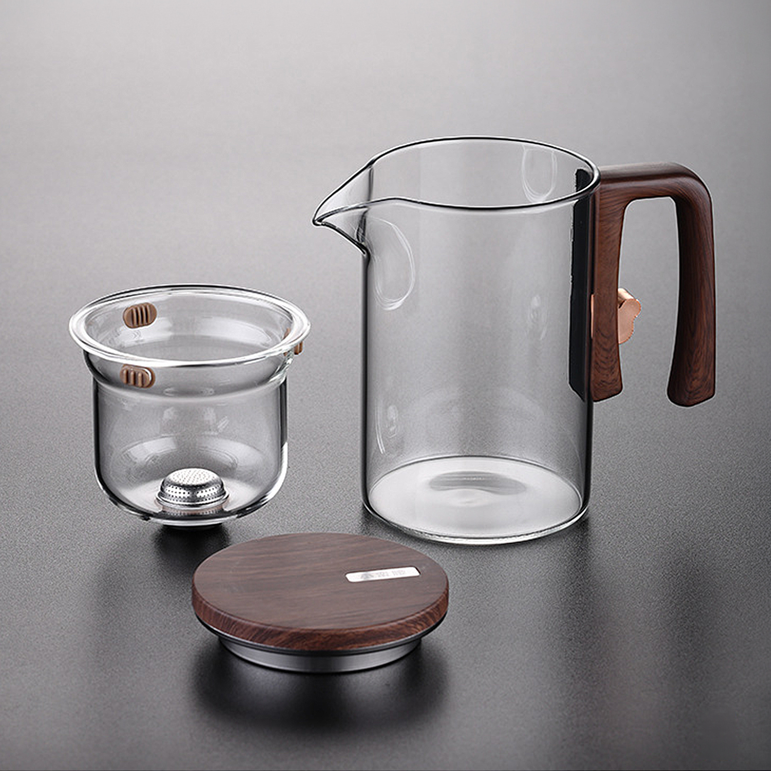 Tetera de cristal con asa de madera, filtro y tapa sobre fondo gris.
