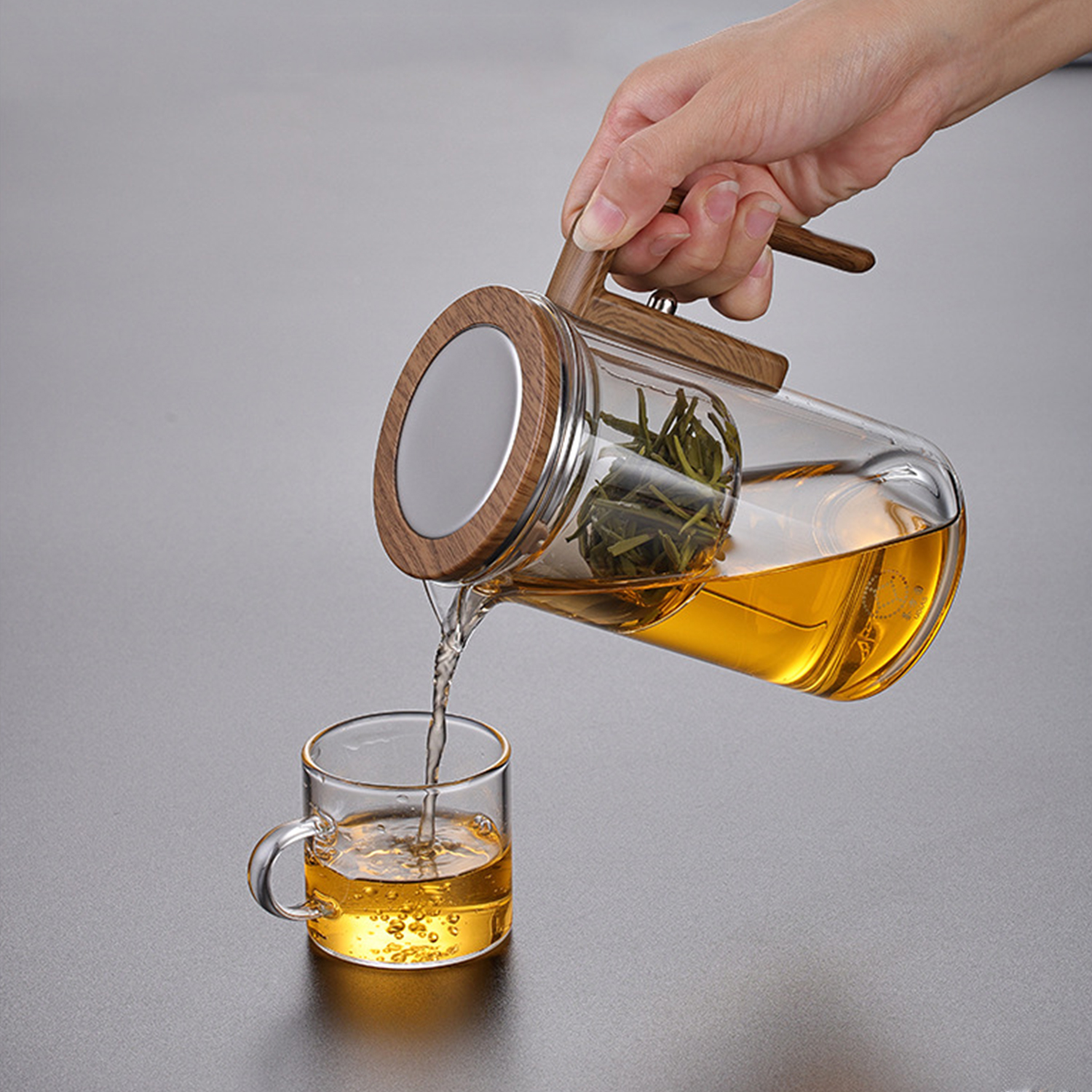 Una mano vierte té de una tetera de cristal con mango de madera en una taza.