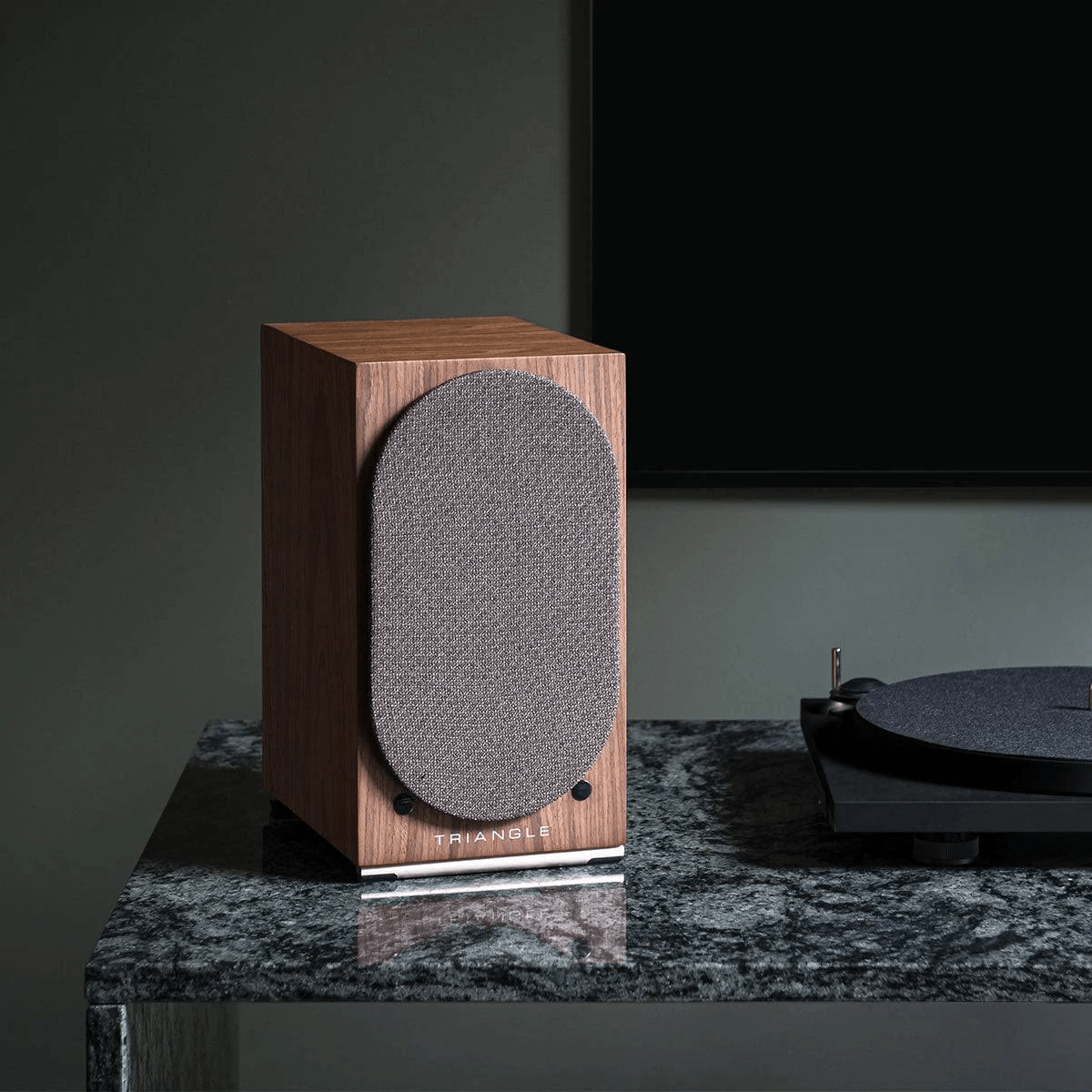 Un altavoz de madera de la marca Triangle descansa sobre una mesa de mármol oscuro junto a un plato giradiscos.