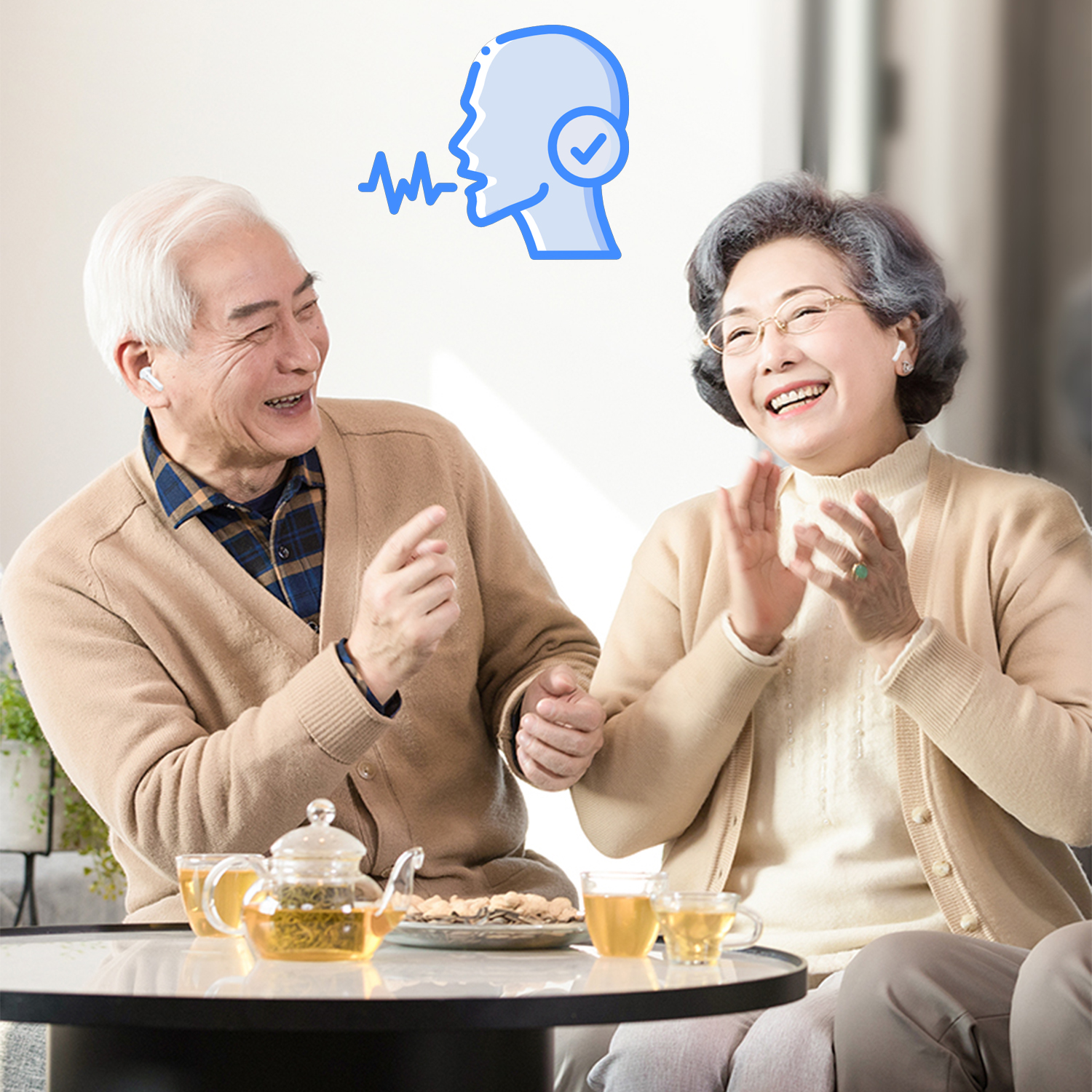 Pareja mayor sonriendo en una mesa con tetera, un icono de voz azul flota de fondo.
