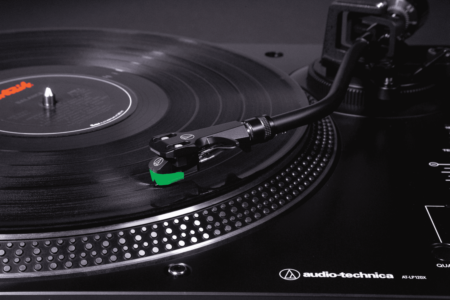 Un tocadiscos negro reproduce un disco de vinilo, con el brazo y la aguja verde apoyados en el surco.