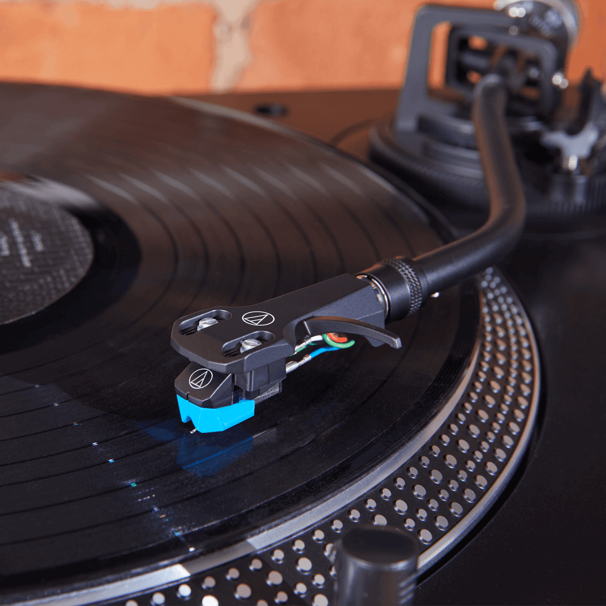Ein Plattenspieler mit schwarzer Vinylplatte und blauer Tonabnehmernadel spielt Musik ab.